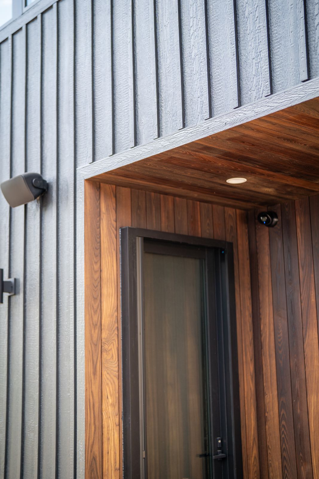 Detail of black siding meeting warm thermally modified wood at the home's entry