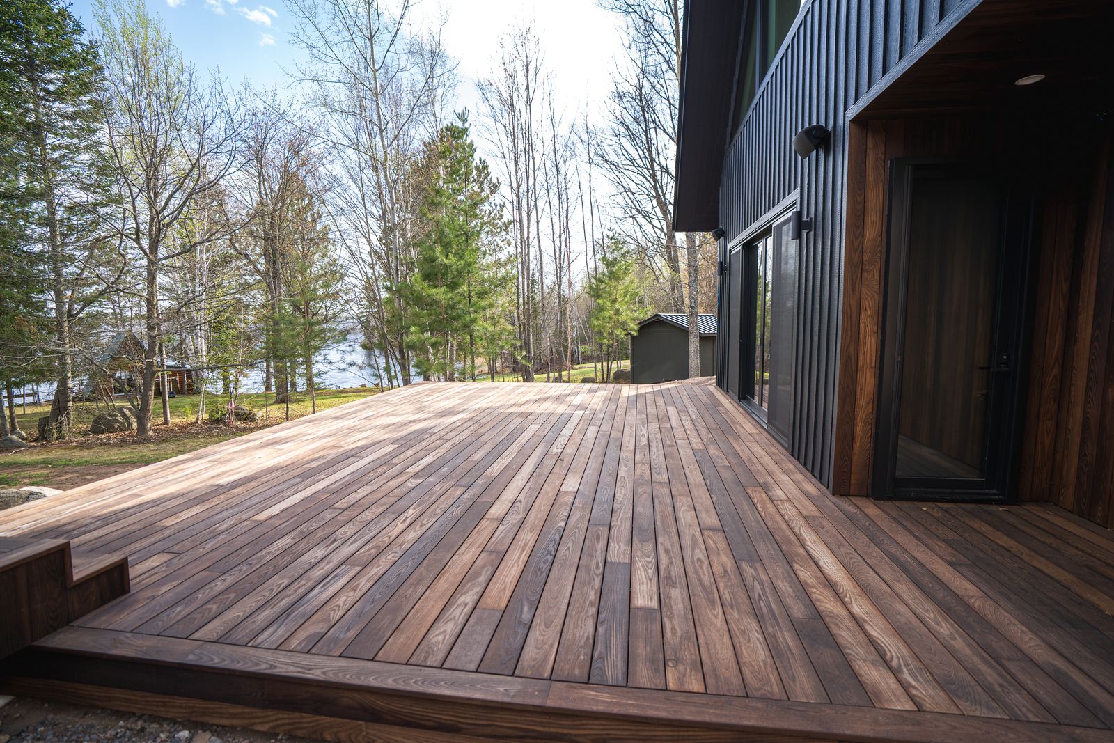 Thermally modified wood deck running alongside the black-sided Island Lake custom home toward the lake
