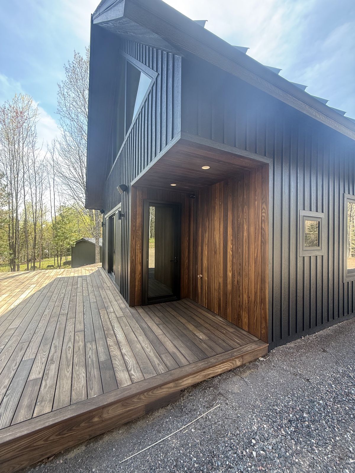 Front entry of the Island Lake custom home — black board-and-batten siding opening into a warm thermally modified wood alcove