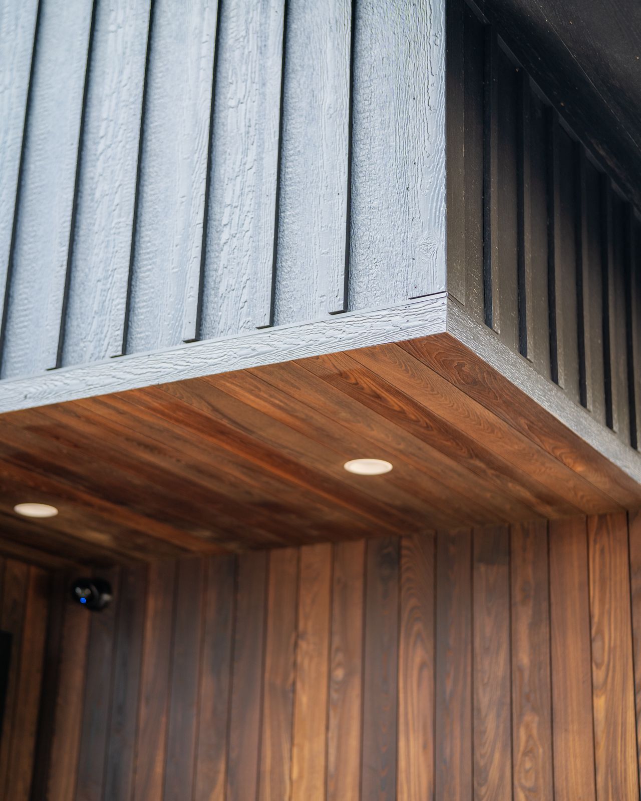 Thermally modified wood soffit with recessed lighting against black board-and-batten siding
