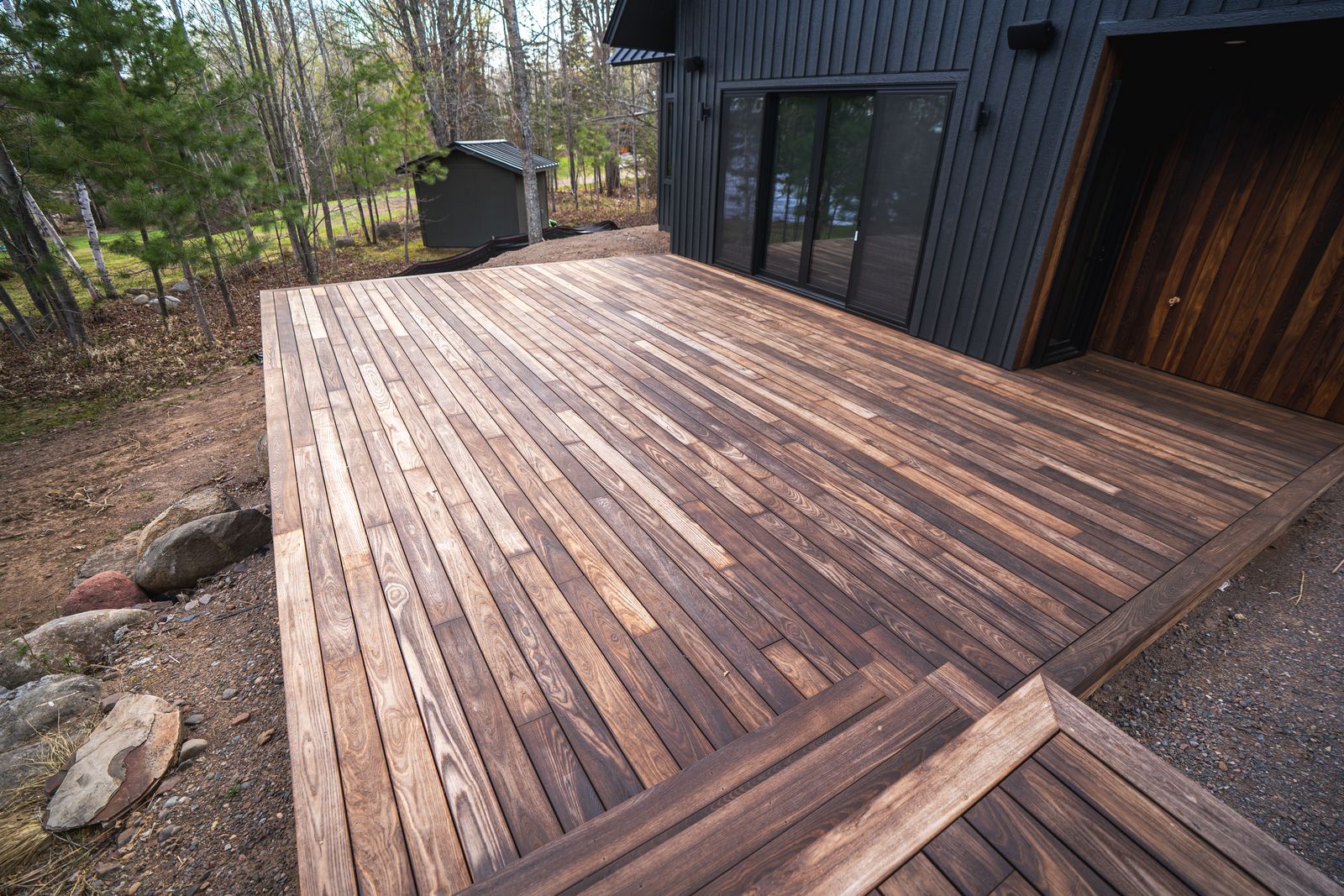 Thermally modified wood deck wrapping the corner of the house down to landscaped boulders